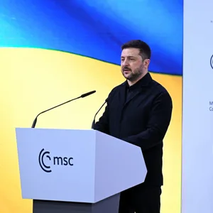 Mann mit Bart an Rednerpult vor gelb-blauer Wand