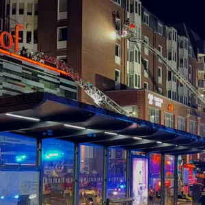 Einsatzkräfte der Feuerwehr sind auf Drehleitern an einem Wohnhaus neben dem Einkaufszentrum Sophienhof im Einsatz.