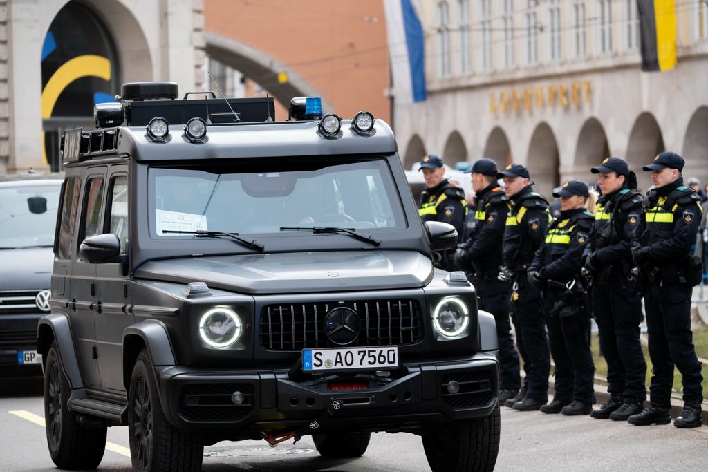 Ein gepanzertes Fahrzeug steht neben einer Reihe Polizist:innen.