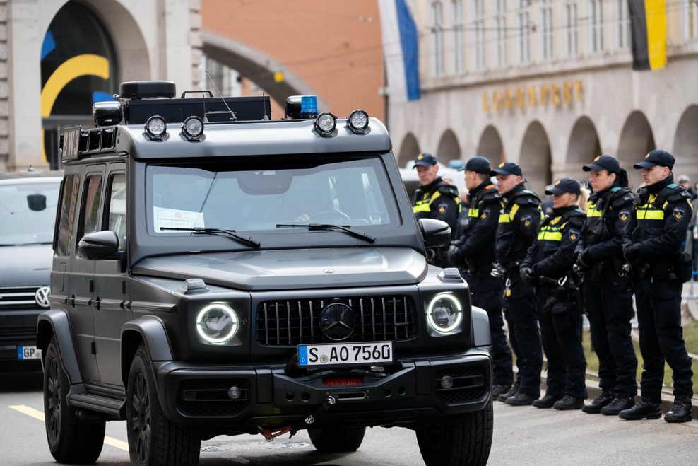 Ein gepanzertes Fahrzeug steht neben einer Reihe Polizist:innen.