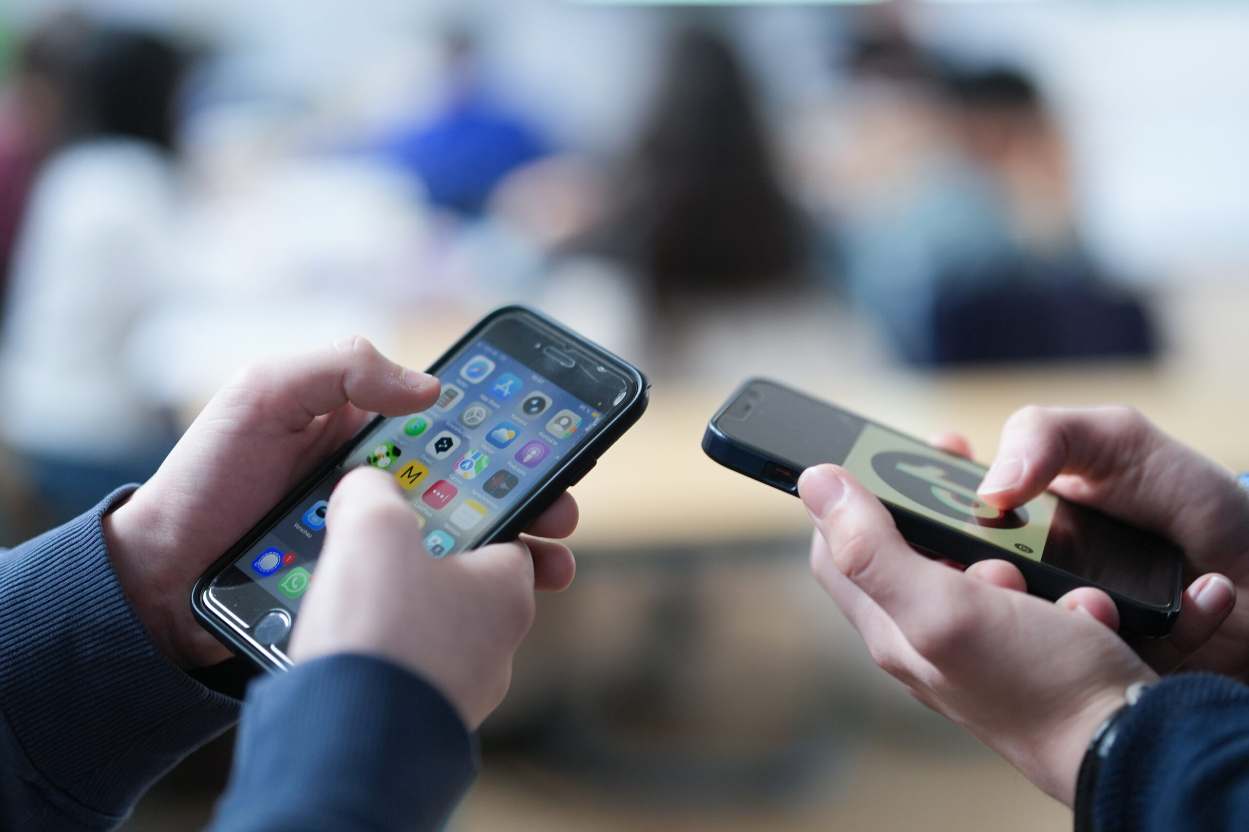 Zwei Schüler schauen auf ihre Smartphones, auf einem der Displays ist das Logo der Social-Media-Plattform TikTok zu sehen.