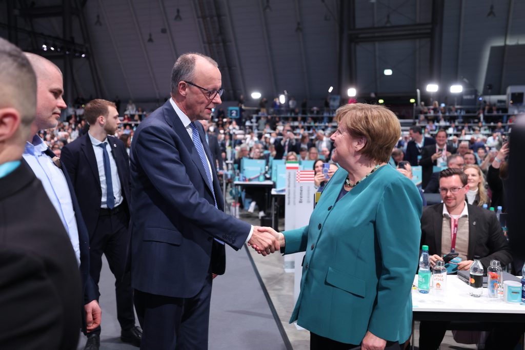 Merz schüttelt Merkel die Hand