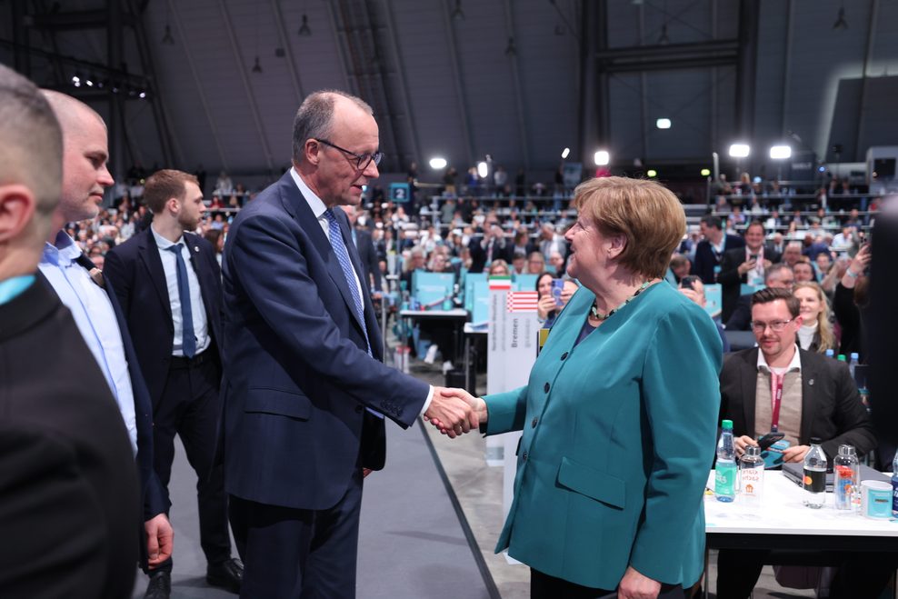 Merz schüttelt Merkel die Hand