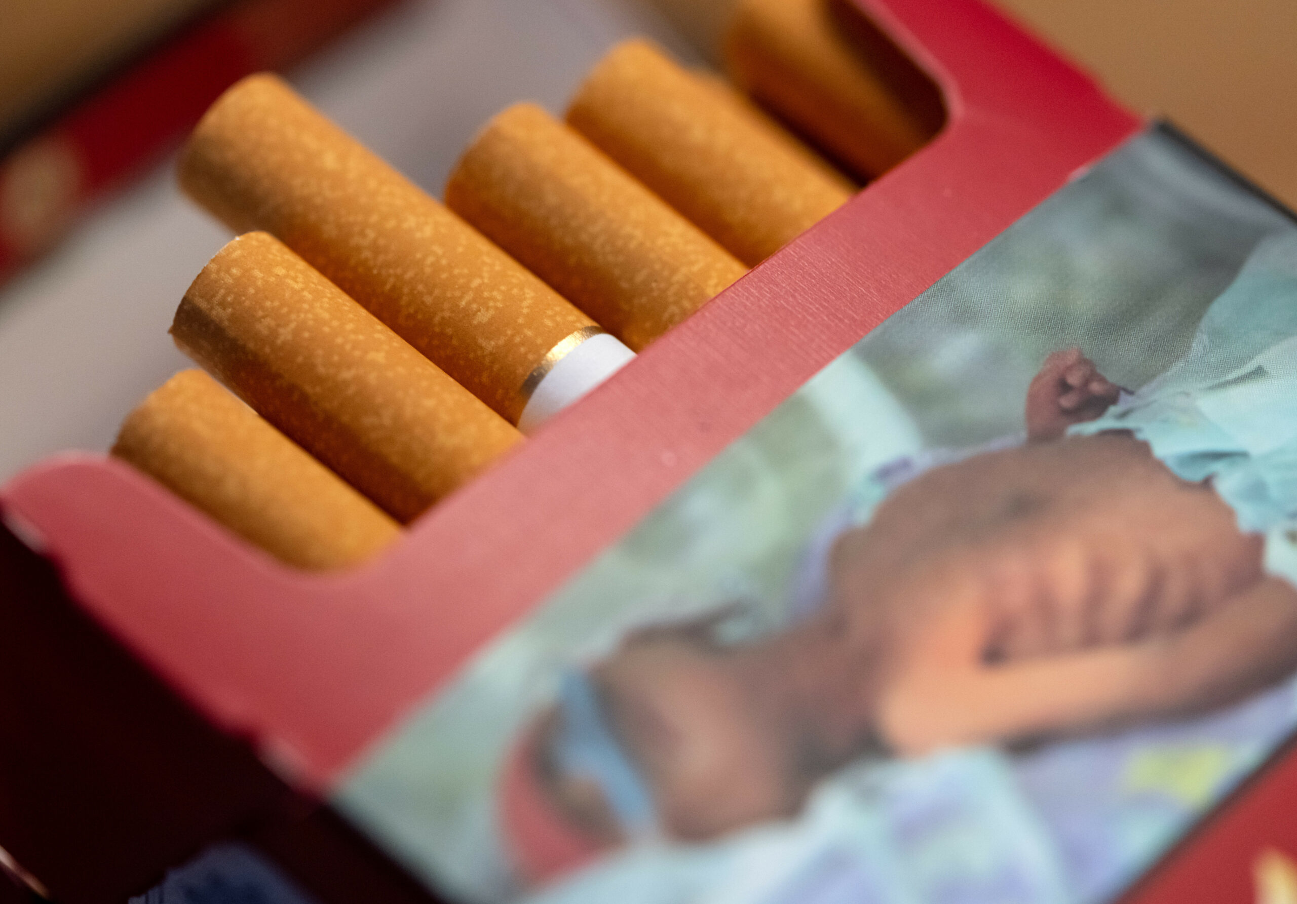 Eine geöffnete Packung Zigaretten mit Schockfoto liegt auf einem Tisch. (Symbolfoto)