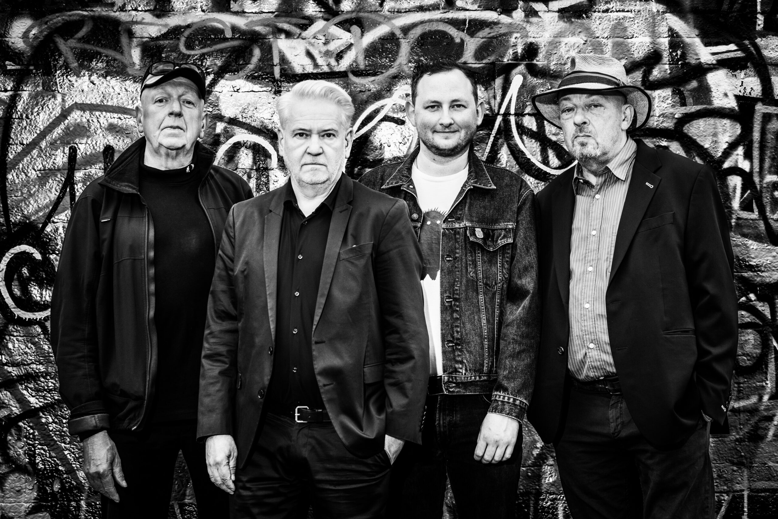 Vier Männer stehen vor einer mit Graffiti besprühten Wand.