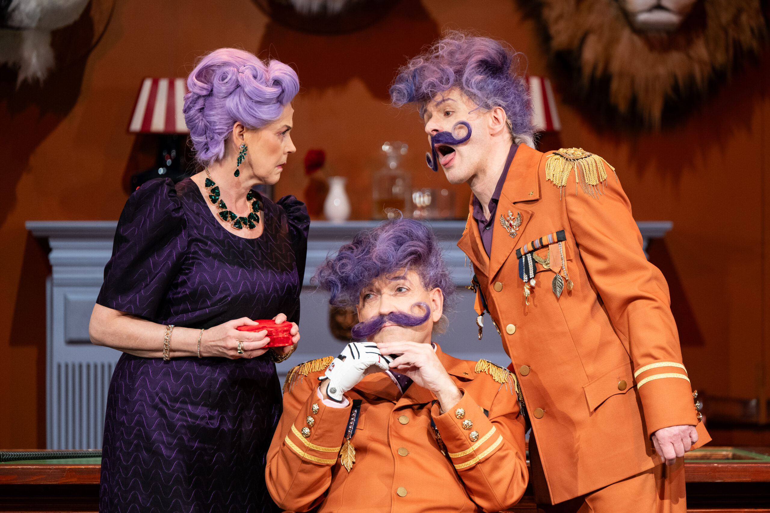 Zwei Männer mit lilafarbenen Haaren und Schnurrbärten tragen orangene Uniformen.