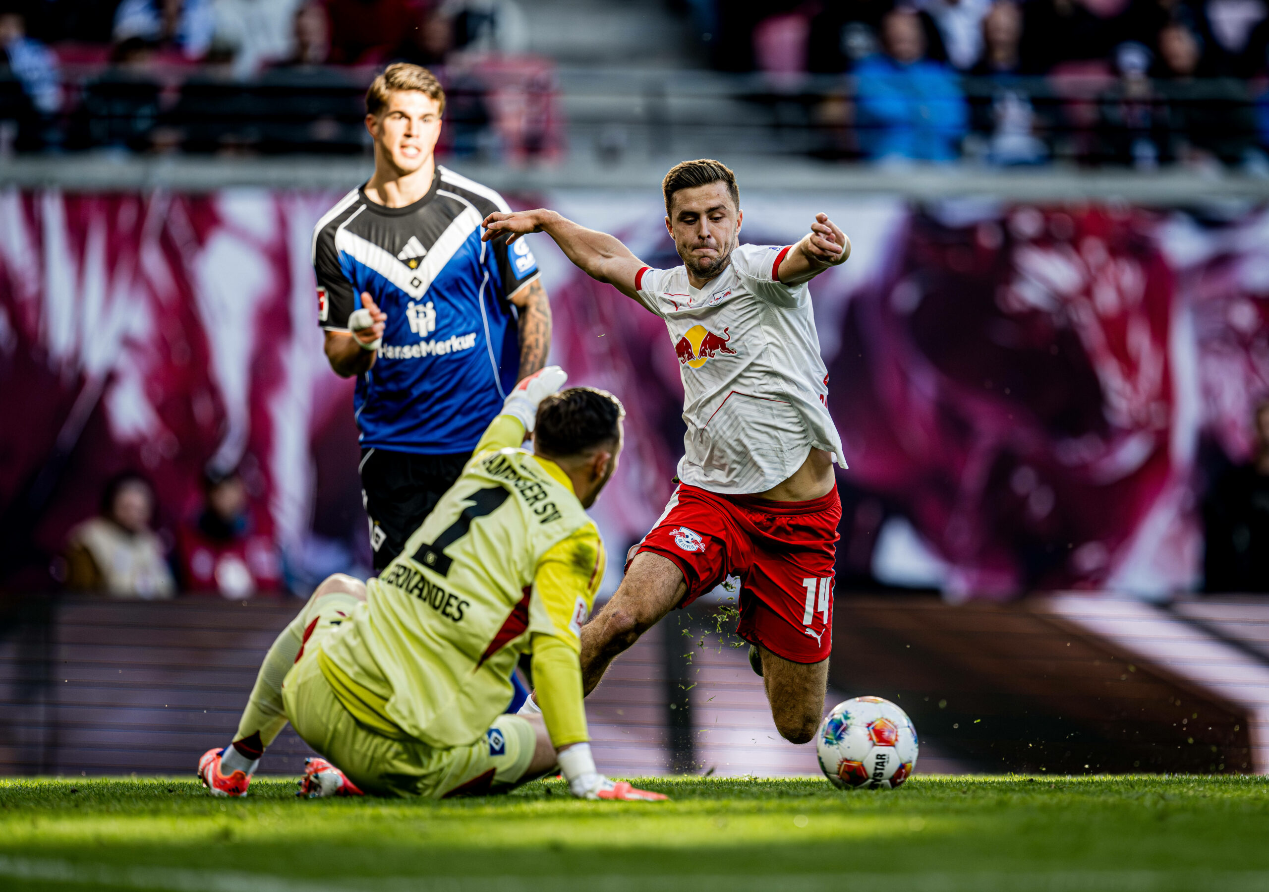 HSV-Torhüter Daniel Heuer sitzt am Boden, Leipzigs Christoph Baumgartner setzt zum Schuss an. Im Hintergrund steht Luka Vuskovic.