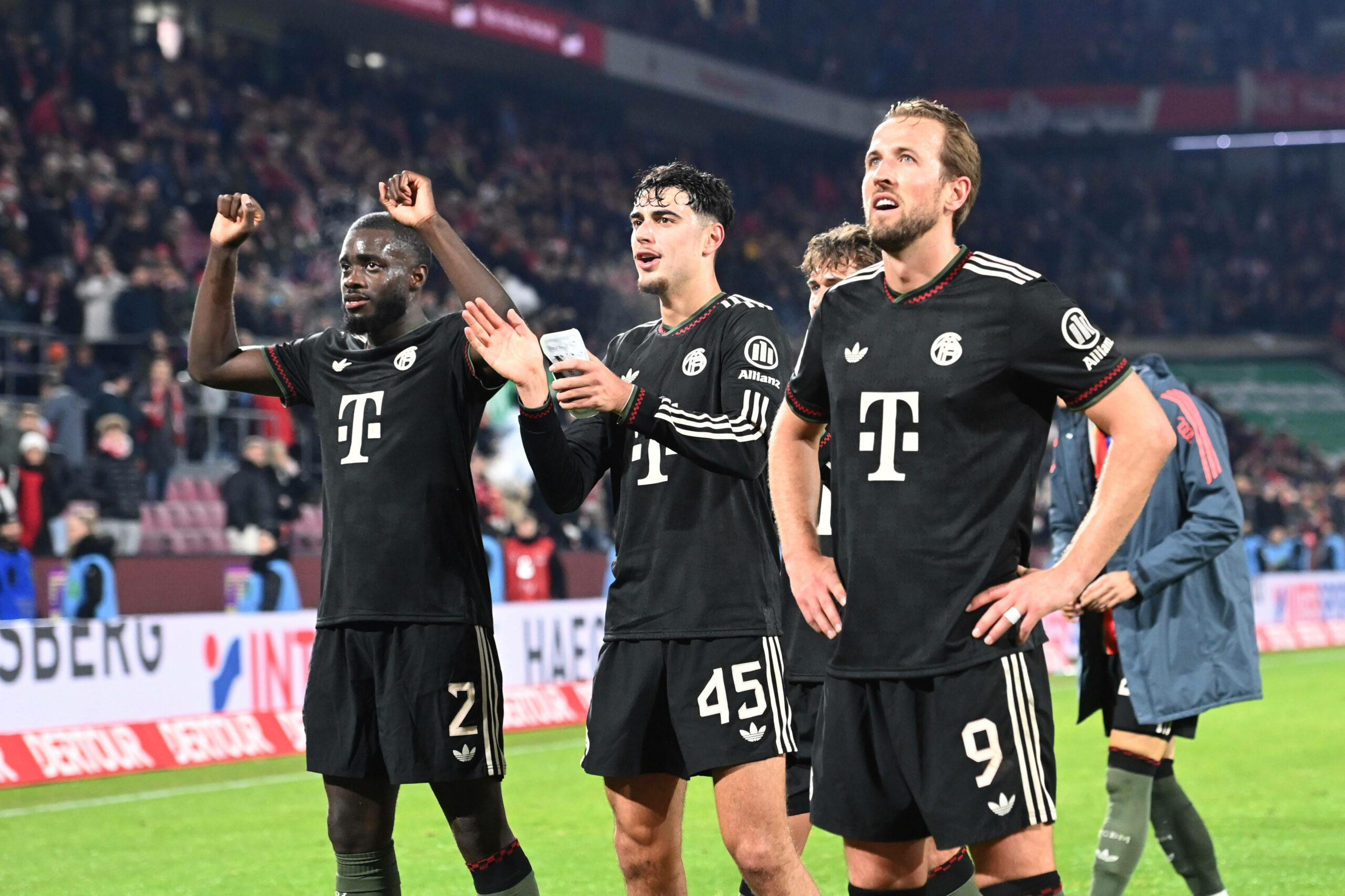 Dayot Upamecano feiert gemeinsam mit Aleksandar Pavlovic und Harry Kane vor dem Bayern-Fanblock.