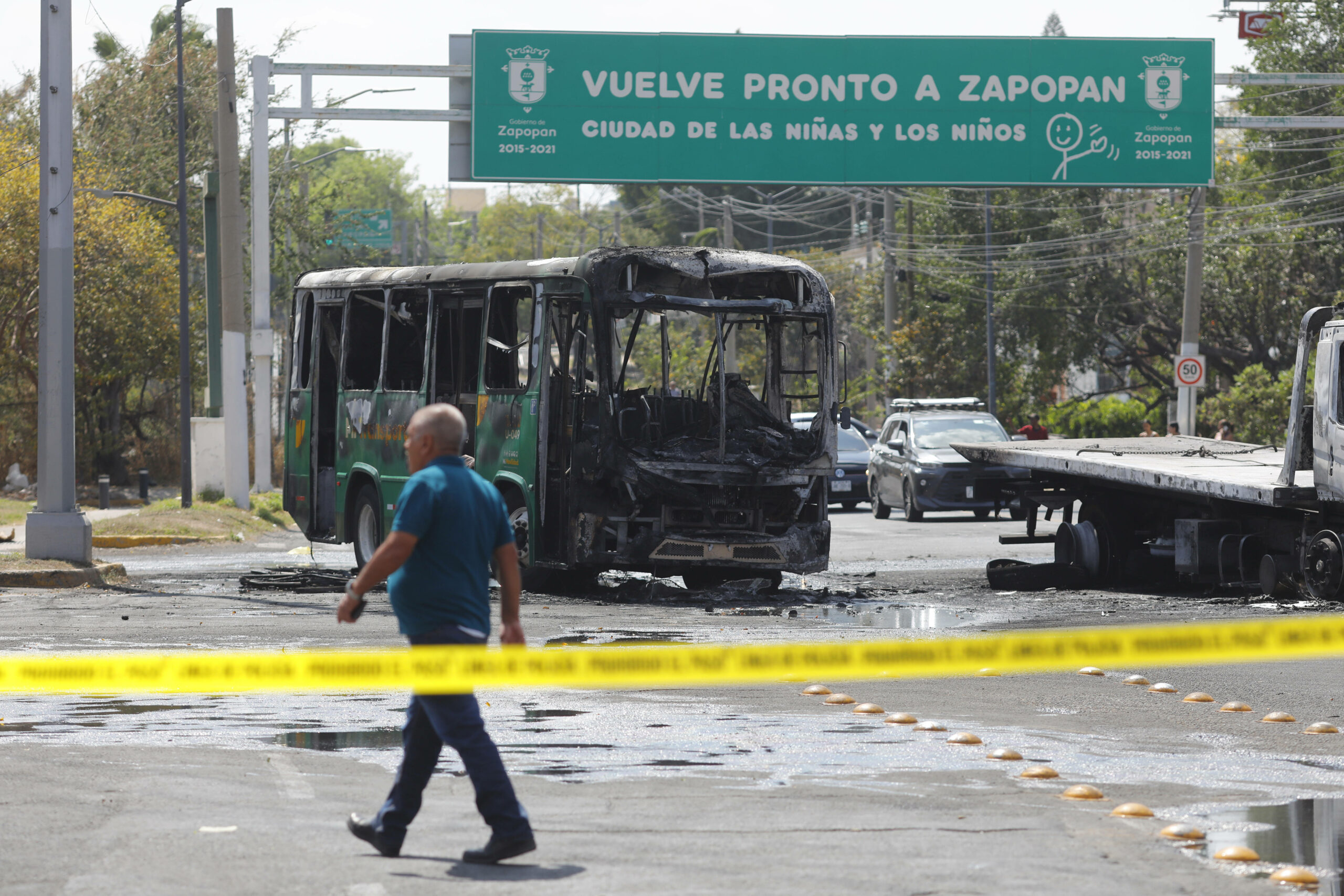 Ein ausgebrannter Bus steht vor einem Ortsschild, das die Stadt als „Die Stadt der Jungen und Mädchen bezeichnet.“