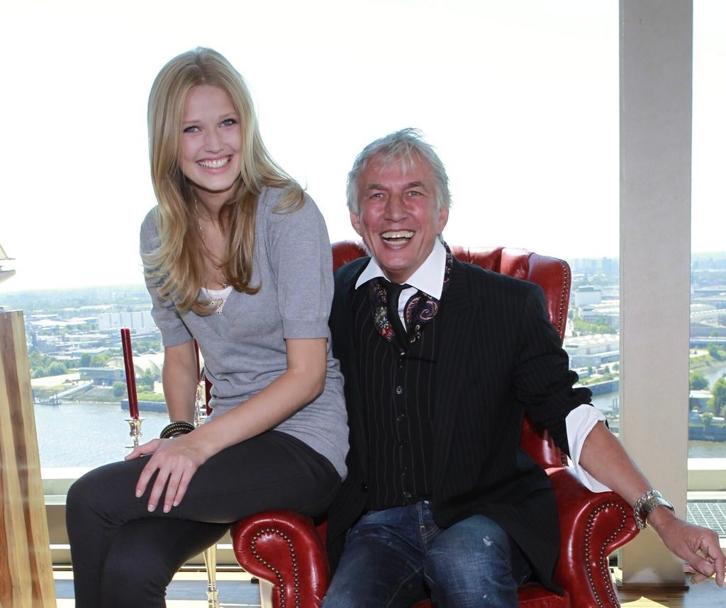 Supermodel Toni Garrn und Ted Linow bei einem Foto-Shooting 2010. Er sitzt auf einem roten Sessel, sie auf einer Armlehne. Beide lachen.