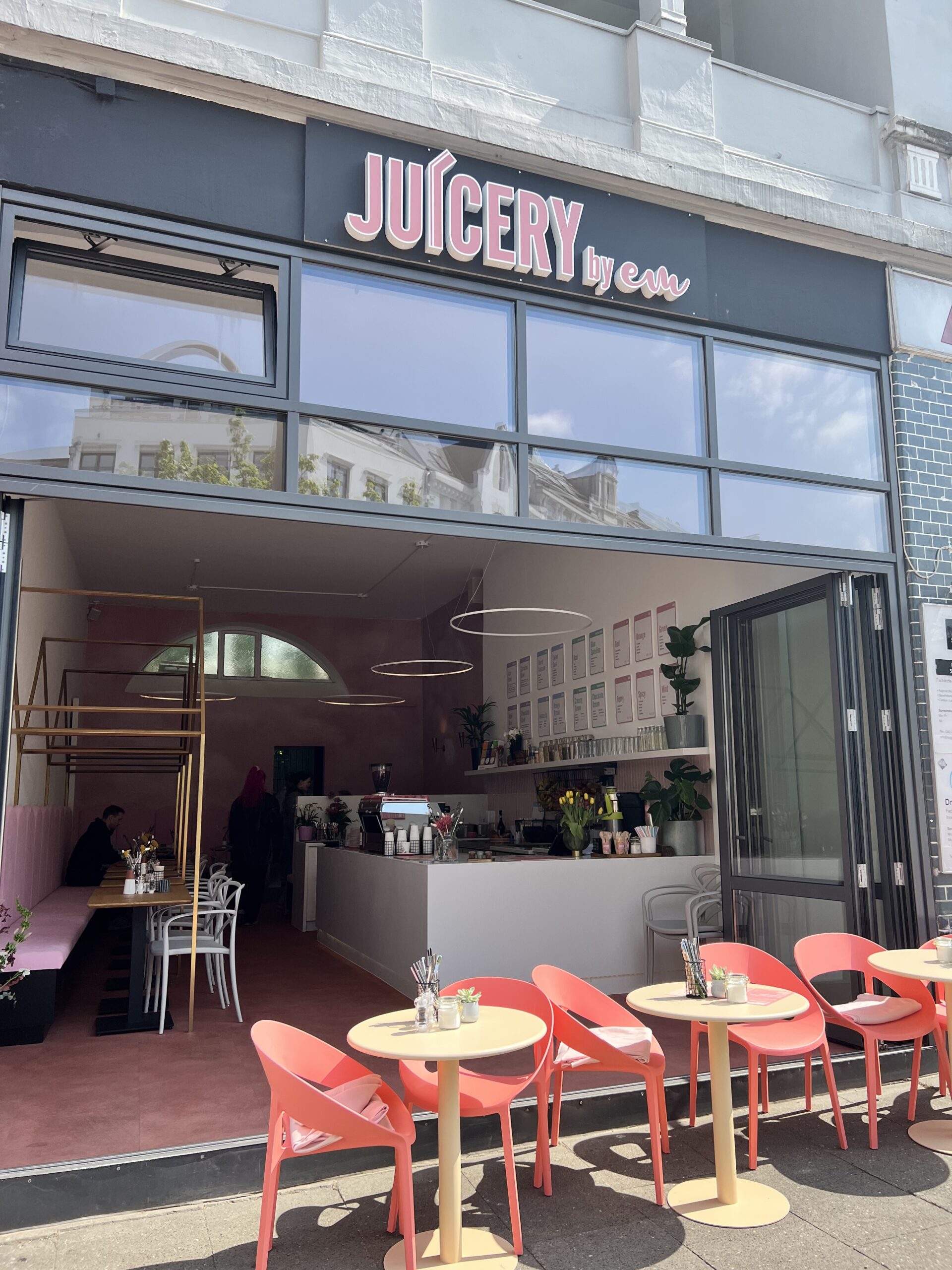 Laden „Juicery by em“ mit roten Stühlen in der offenen Tür