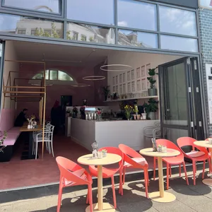 Laden „Juicery by em“ mit roten Stühlen in der offenen Tür