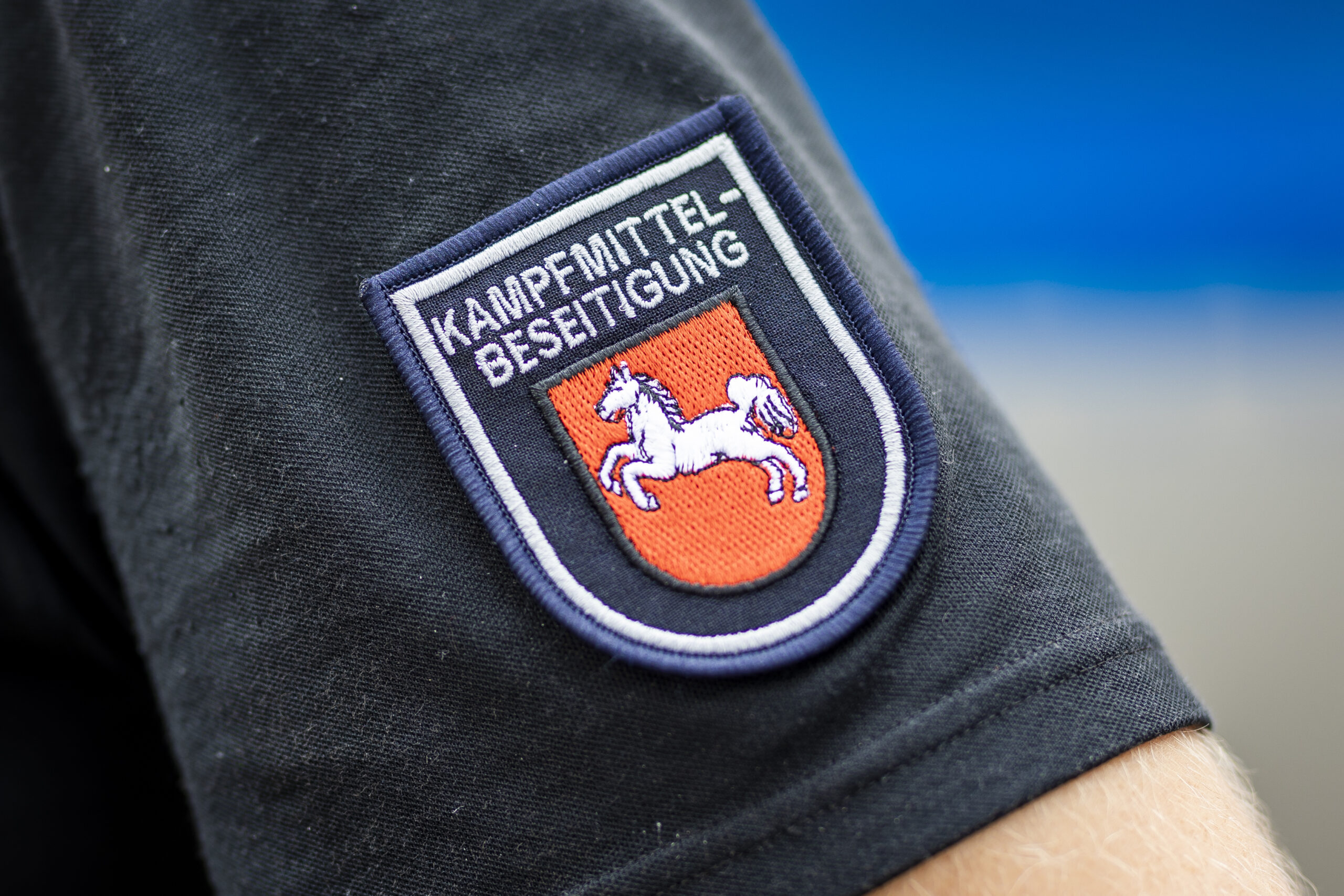Der Schriftzug „Kampfmittelbeseitigung“ ist an einem Ärmelabzeichen eines Mitarbeiters vom Kampfmittelbeseitigungsdienst (KBD) Niedersachsen zu lesen.