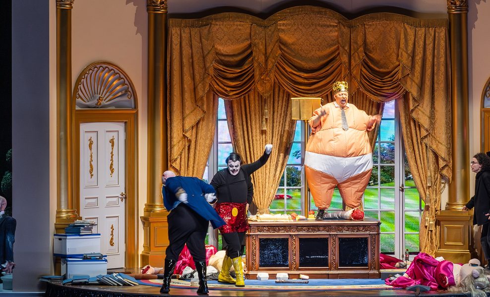 Ein Raum mit goldenen Möbeln, goldenem Vorhang, goldenen Säulen. Auf einem goldenen Schreibtisch steht die Figur des Präsidenten in einem aufblasbaren Nackt-Kostüm, das ihn in weißer Unterhose zeigt