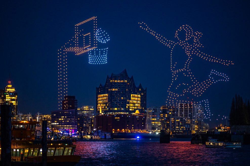 Spektakel über dem Hafen: Eine Drohnen-Show lässt eine Basketballerin am Nachthimmel zum Wurf ansetzen – und der Ball landet im Korb.