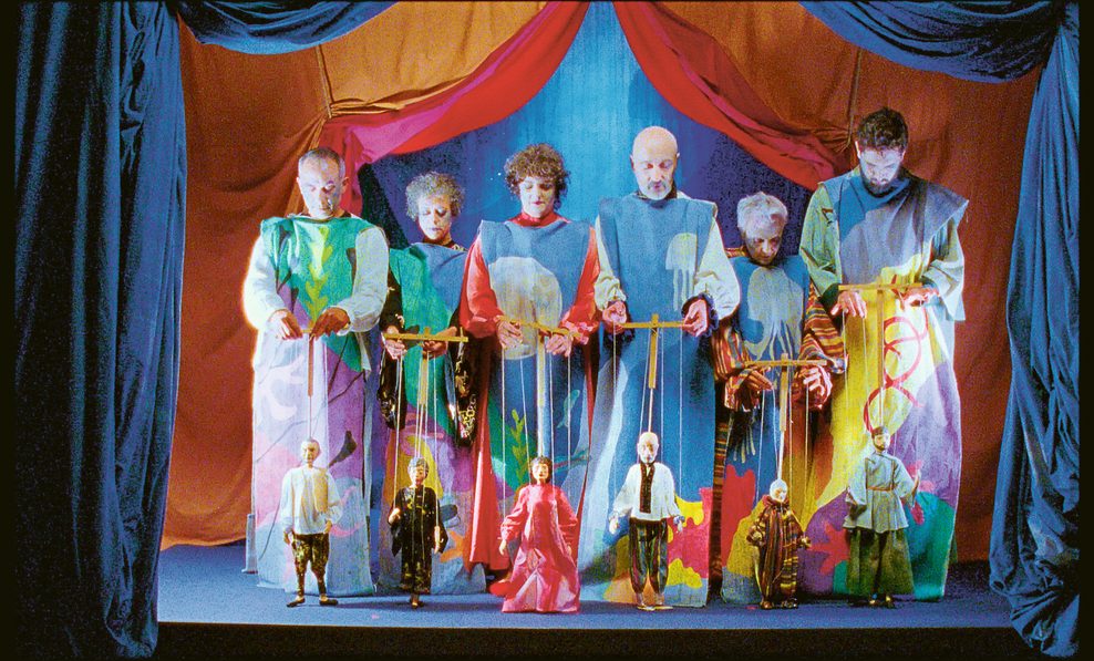 Mehrere bunt gekleidete Puppenspieler in einem bunten Theater