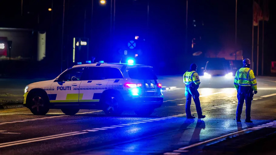 Dänische Polizisten stehen neben einem Polizeiwagen auf der Straße.