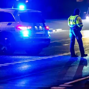 Dänische Polizisten stehen neben einem Polizeiwagen auf der Straße.