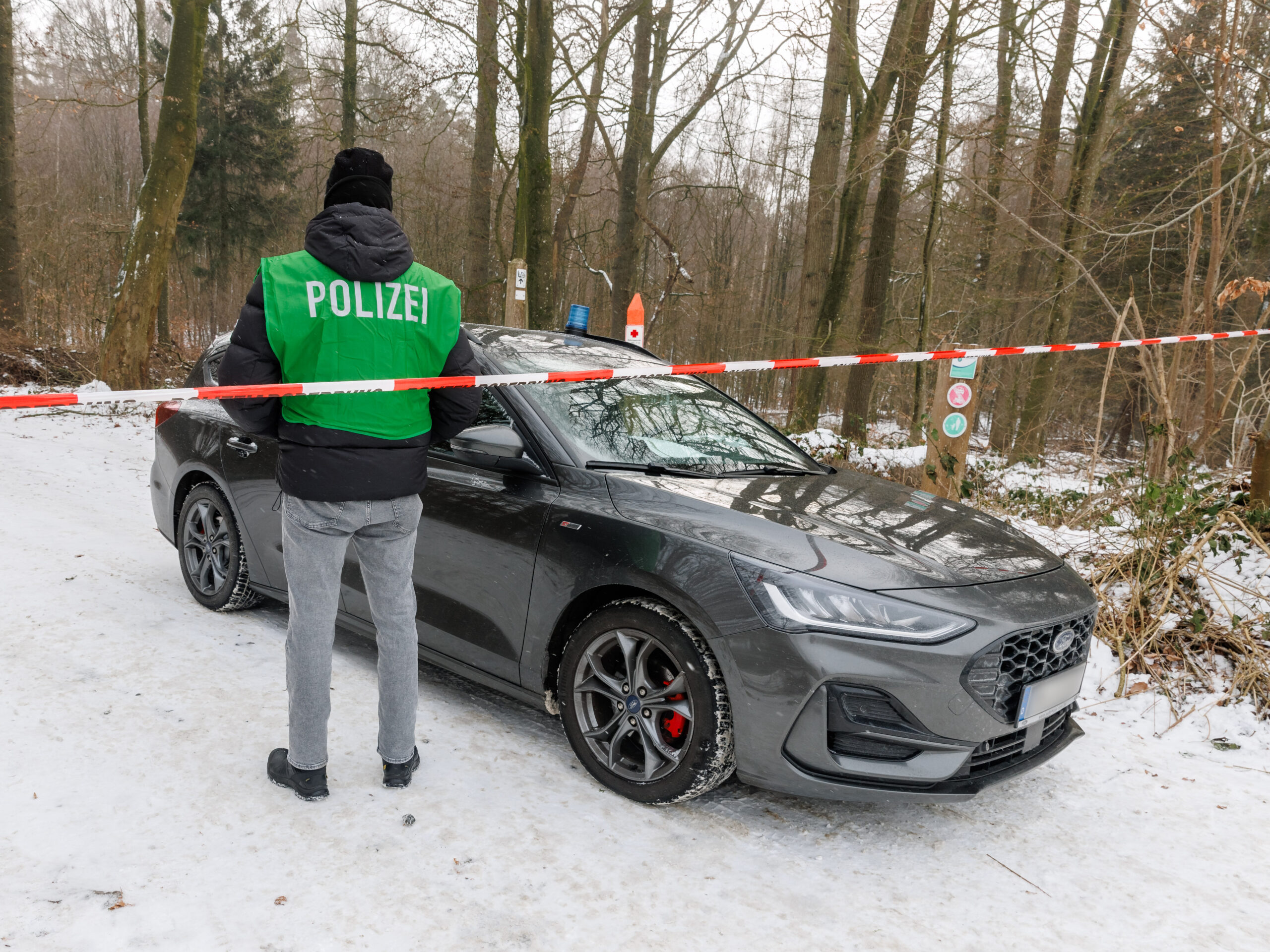 Ein Polizist sperrt die Zufahrt in ein Waldstück. Die Polizei sucht hier mit Leichenspürhunden nach Spuren eines möglichen Verbrechens.