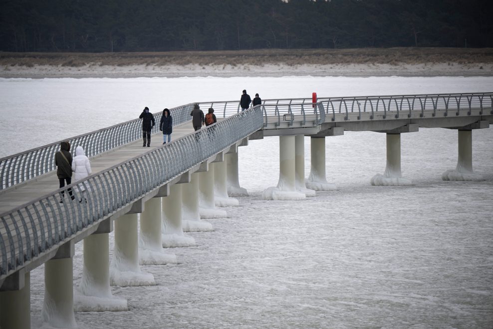 Menschen laufen auf der Seebrücke in Prerow. Die längste Seebrücke an der Ostseeküste ist komplett vom Eis umschlossen.