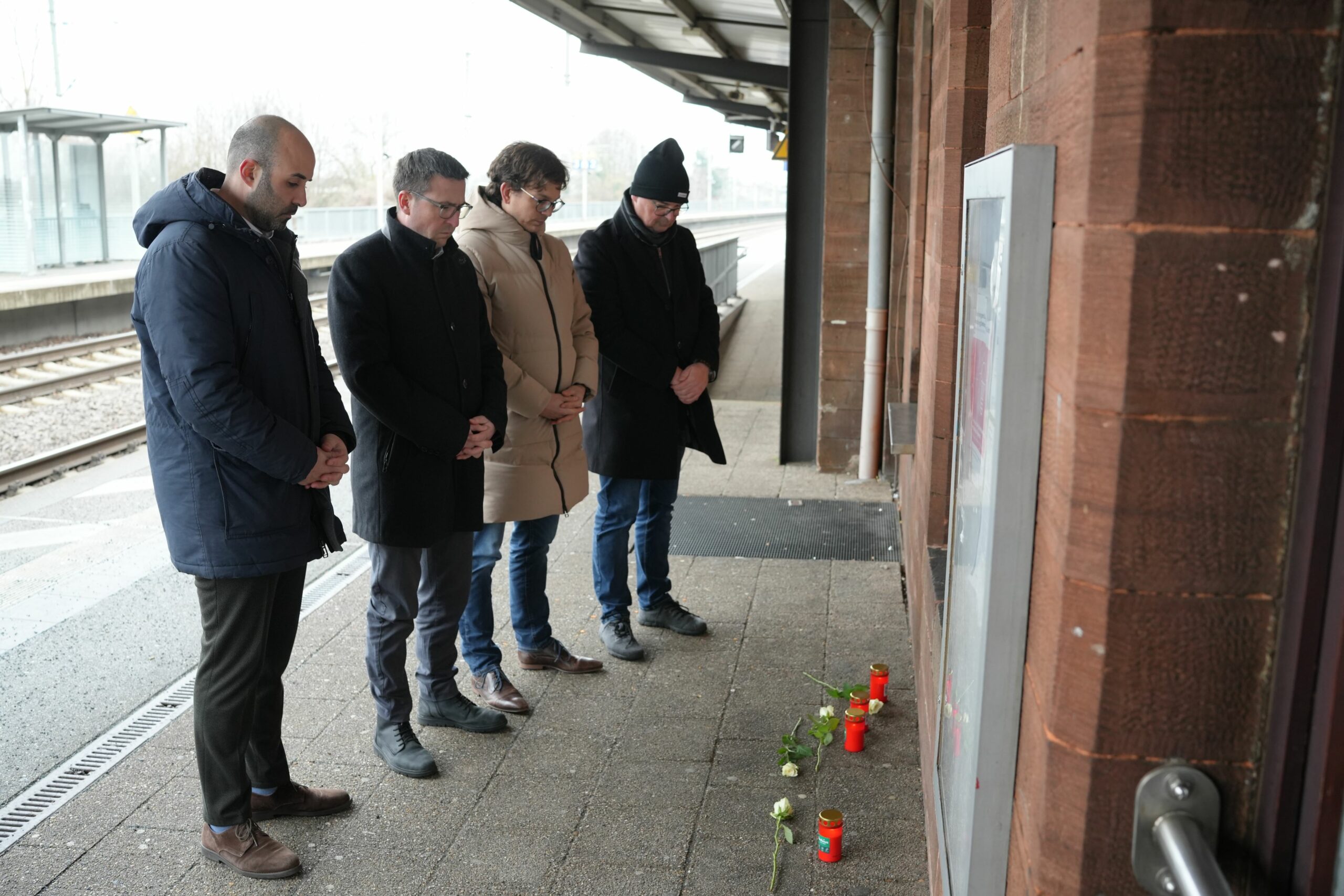 Menschen stehen vor Blumen und Kerzen auf dem Bahnsteig am Bahnhof Landstuhl im Gedenken an den Tod eines Schaffners.