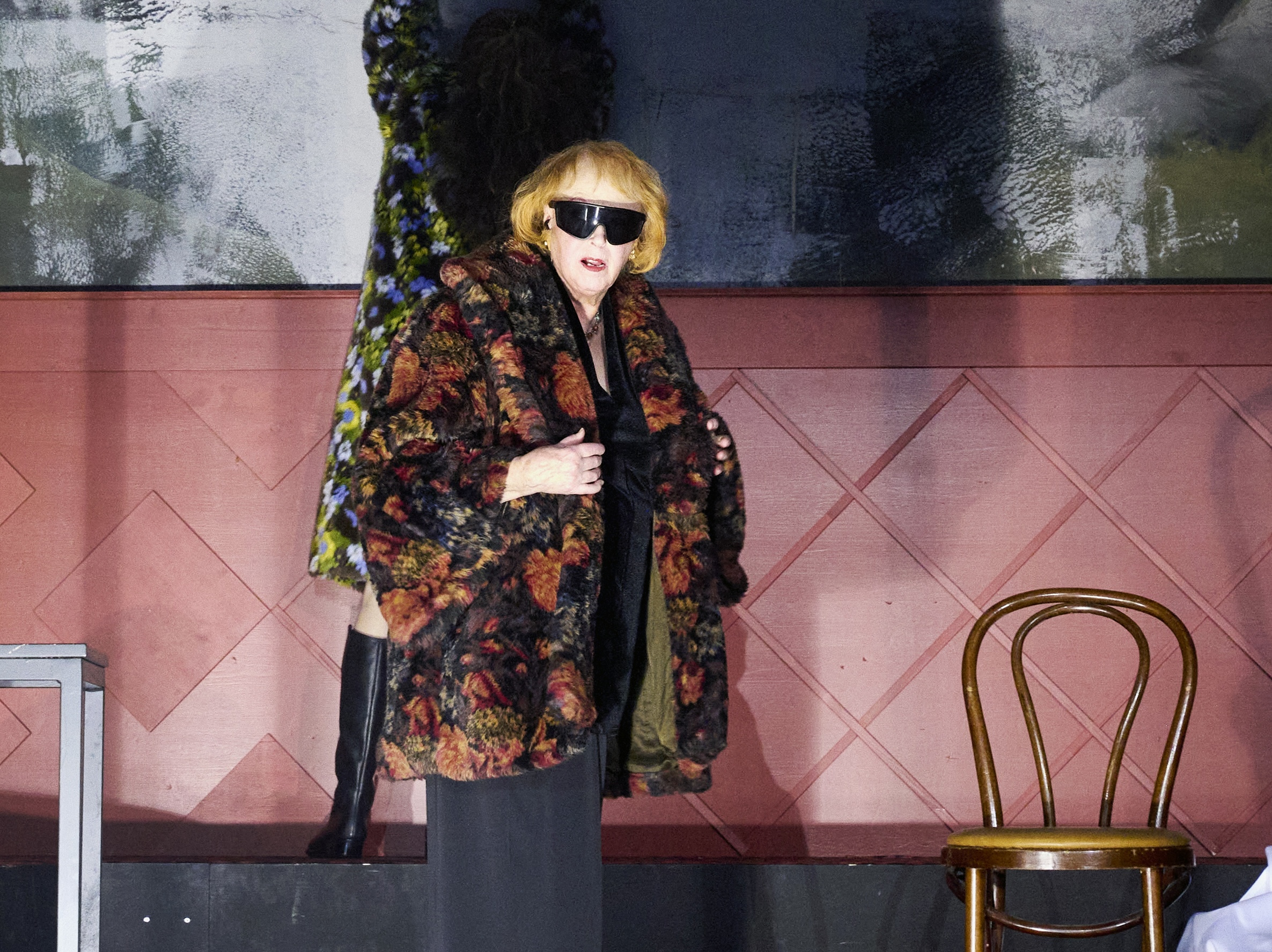 „Alphabet“: Eine Person im gemusterten Mantel und mit Sonnenbrille schaut in Richtung Publikum