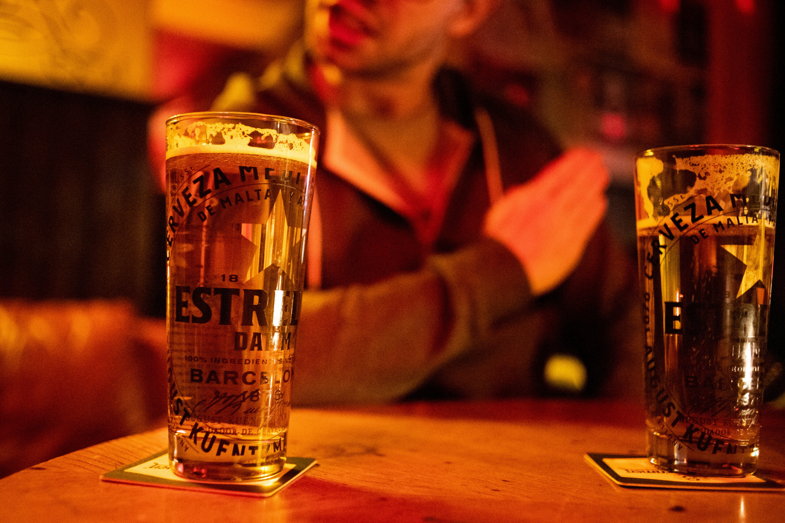 Zwei Bierglaeser stehen in einer Kneipe in Berlin auf dem Tisch, während im Hintergrund ein Mann Streit sucht (Symbolbild).