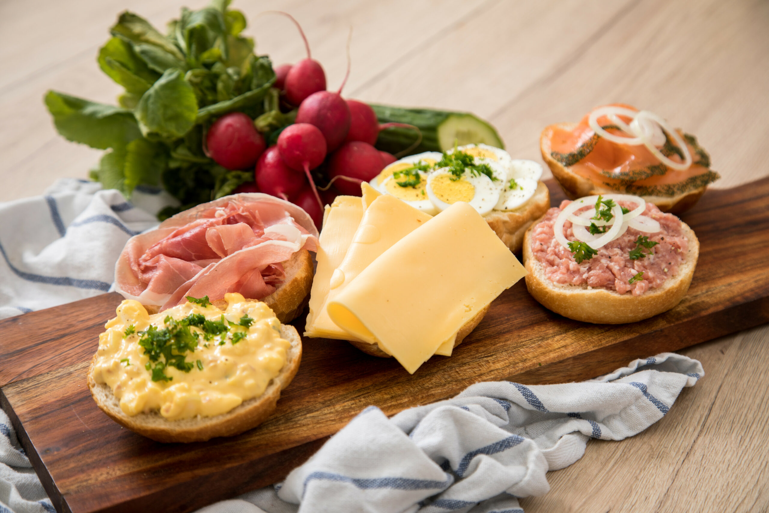 Halbe Brötchen auf einem Brett mit Schinken, Ei, Käse, Mett und Lachs.