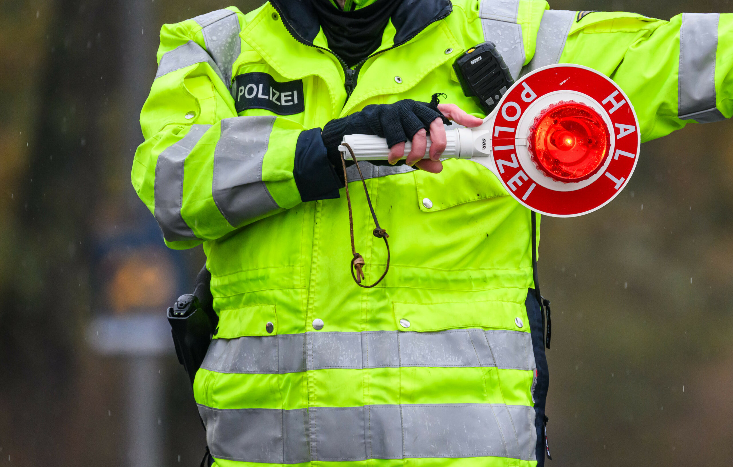 Ein Polizist in gelber Warnjacke hält ein Stopp-Signal in der Hand.