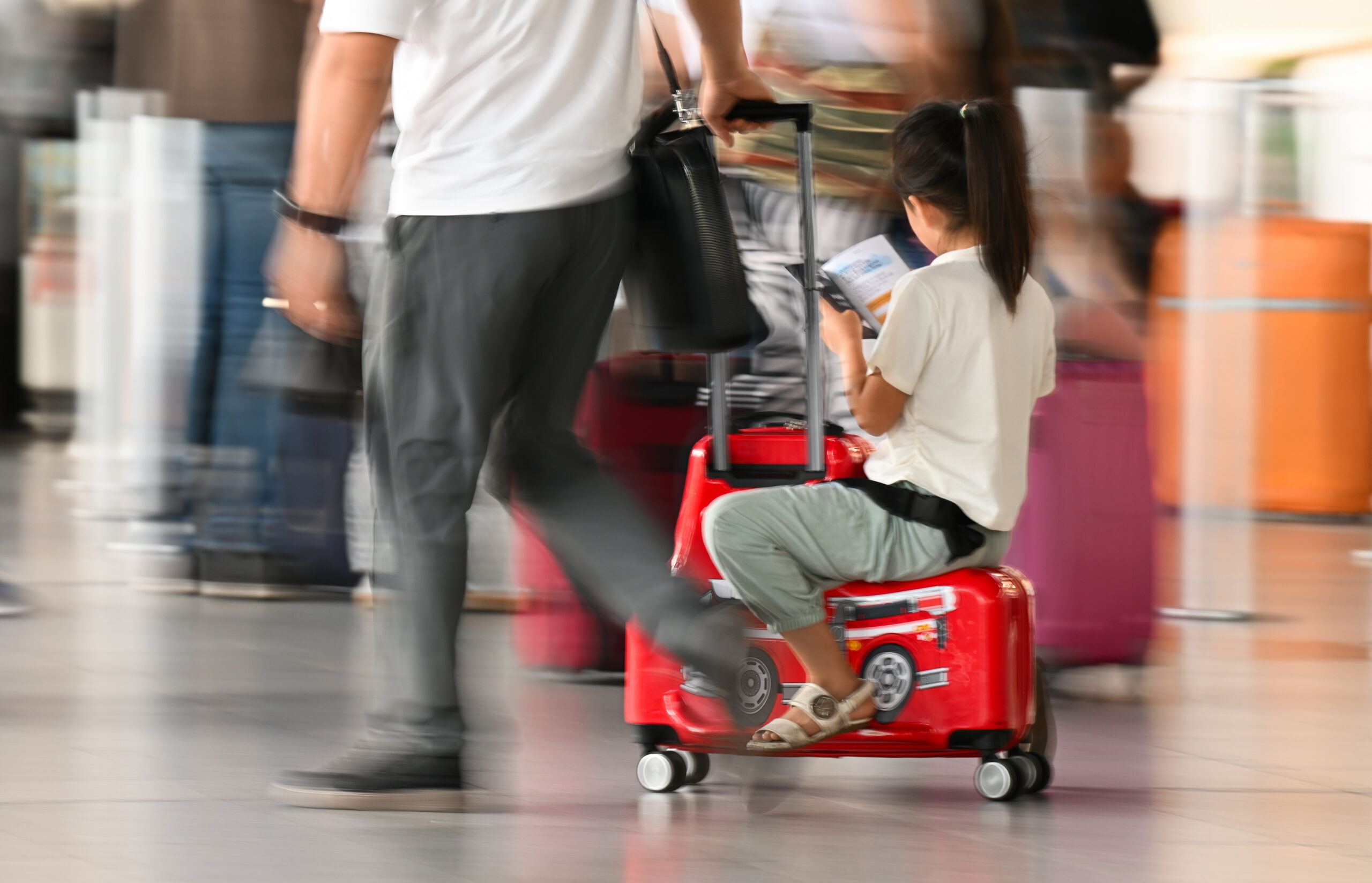 Ein Mädchen sitzt auf einem Koffer und lässt sich durch einen Terminal des Frankfurter Flughafens ziehen.