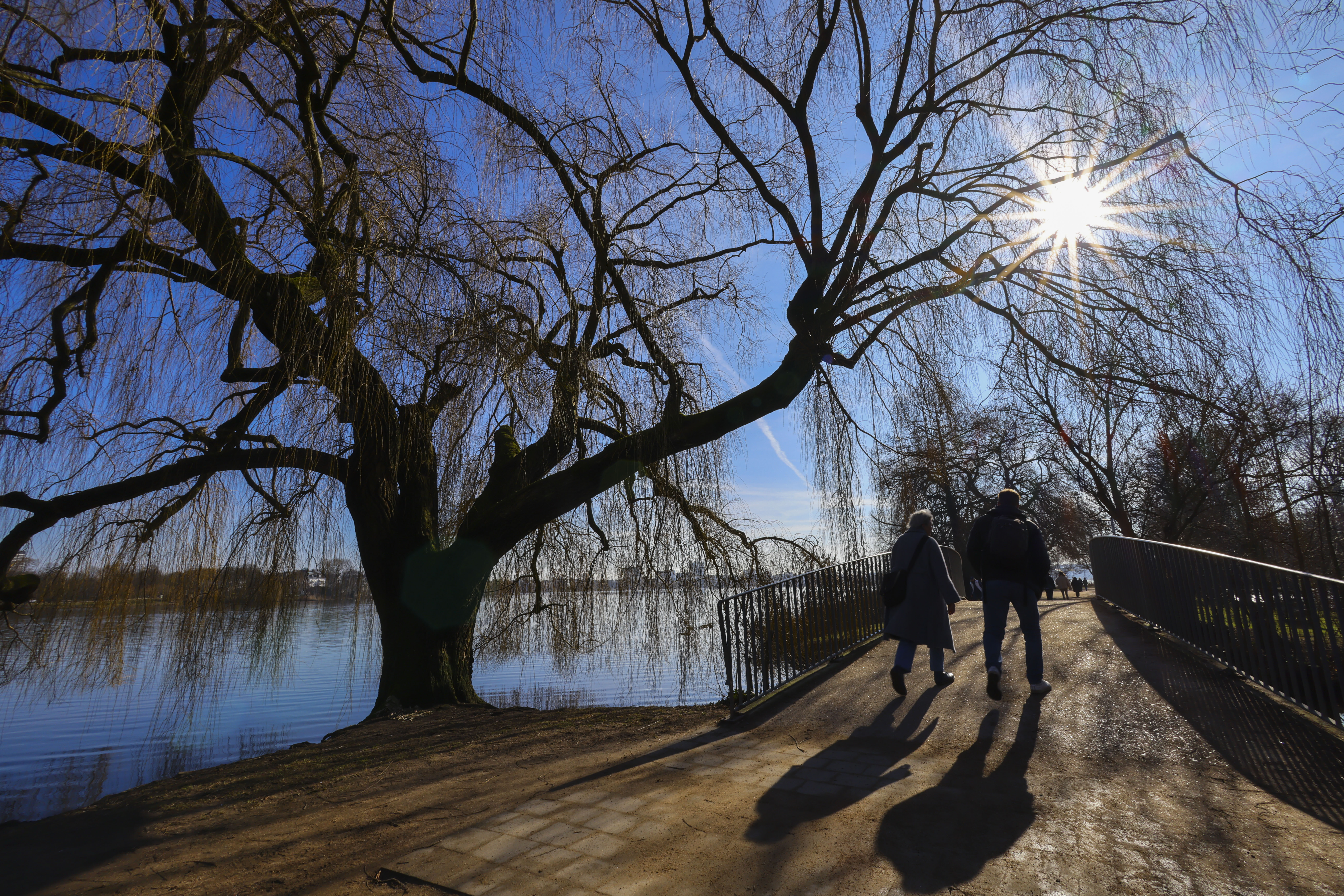 Passanten sind bei strahlendem Sonnenschein und milden Temperaturen an der Alster unterwegs.