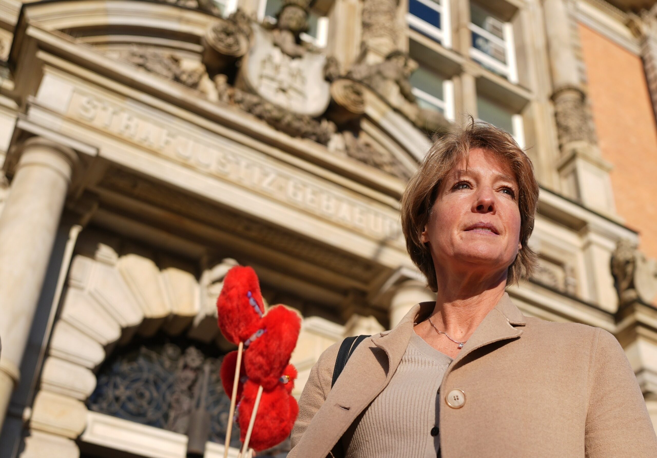 Frau in beigem Mantel vor Gerichtsgebäude