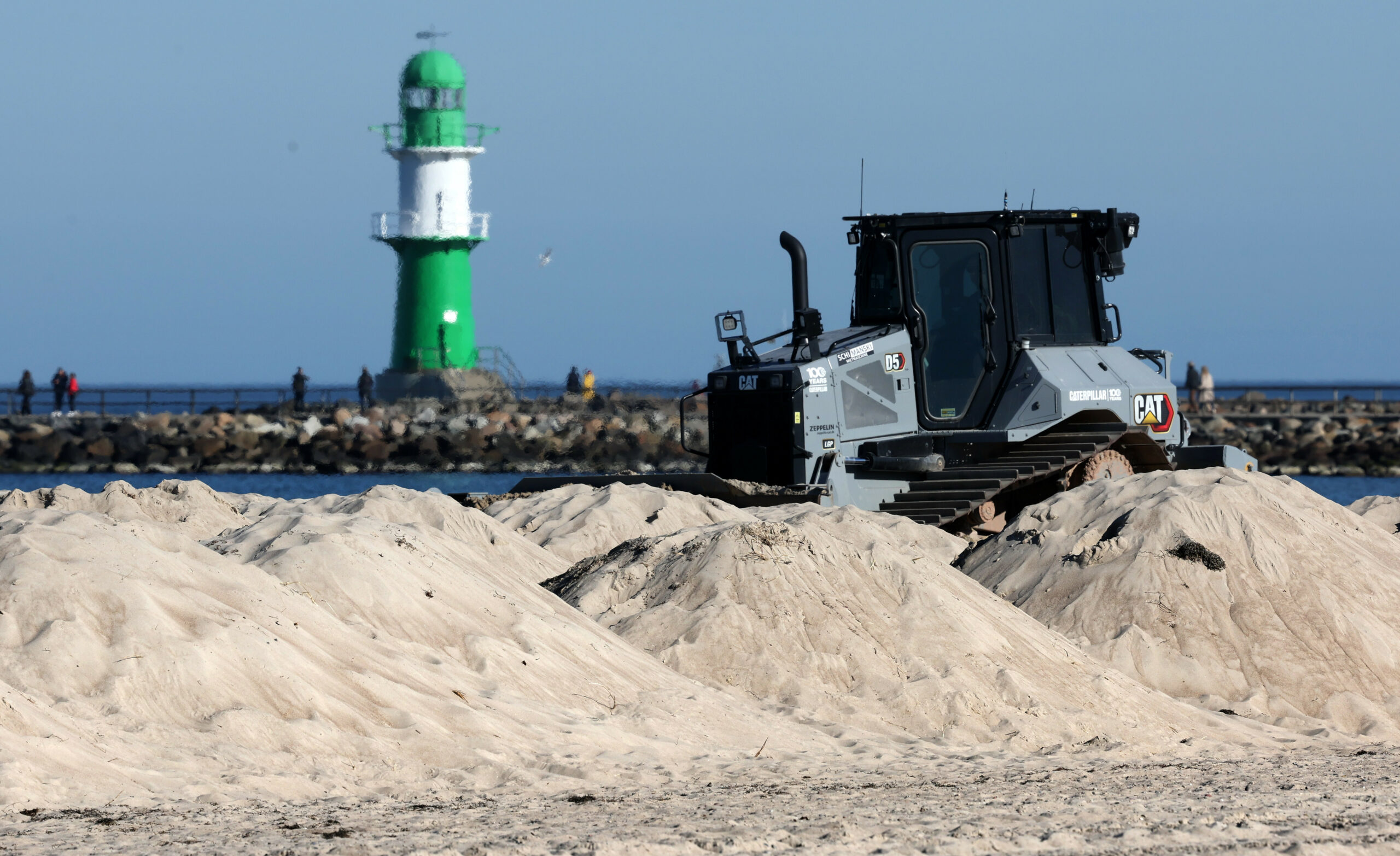 Große Sandhaufen werden am Ostseestrand von einer Planierraupe verteilt.