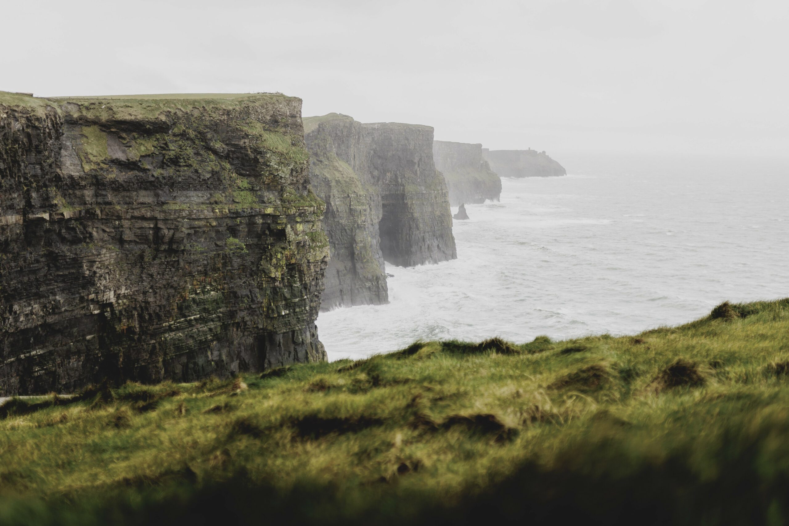 Steile Küsten in Irland. Davor sieht man grüne Flächen.