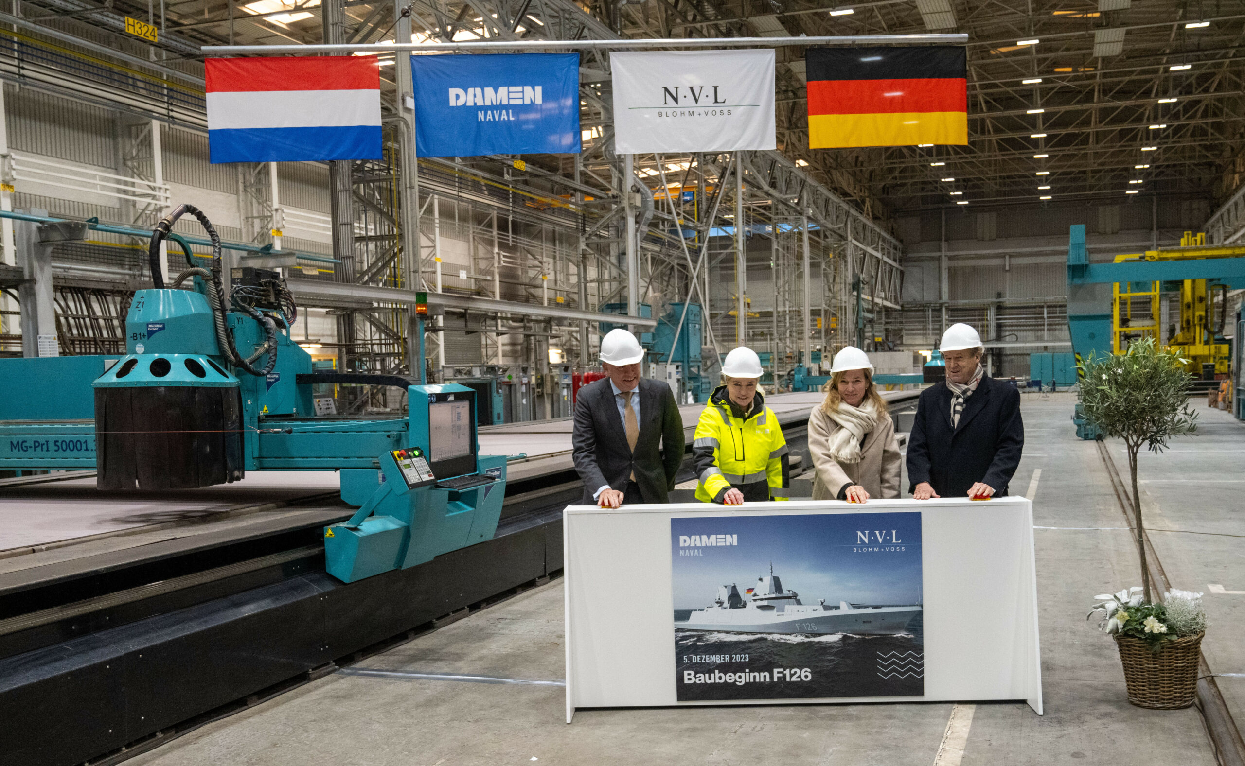 Roland Briene (v.l.), Direktor von Damen Naval, Manuela Schwesig (SPD), Ministerpräsidentin von Mecklenburg-Vorpommern, Siemtje Möller (SPD), Parlamentarische Staatssekretärin beim Bundesminister der Verteidigung und Friedrich Lürßen, Gesellschafter der Unternehmensgruppe Lürssen stehen zum Brennstart der F126-Fregatte in einer Werfthalle.