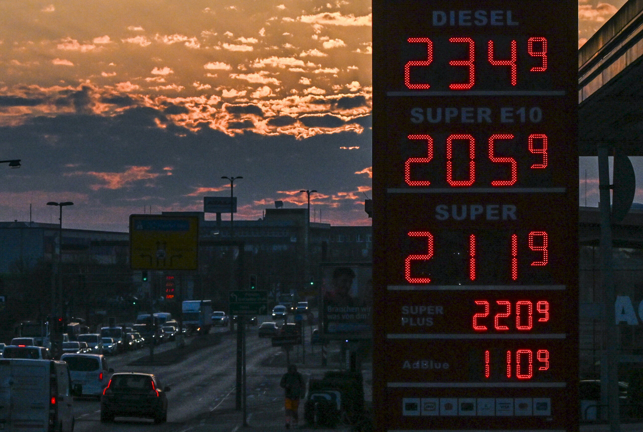 Auf einer Anzeigetafel einer Tankstelle stehen bei Sonnenaufgang die aktuellen Preise für Benzin und Diesel.