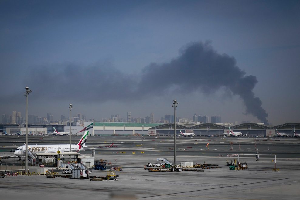 Eine Rauchwolke, verursacht durch einen iranischen Angriff, ist im Hintergrund zu sehen, während Flugzeuge der Emirates nach der Schließung des Flughafens auf dem Dubai International Airport geparkt sind.