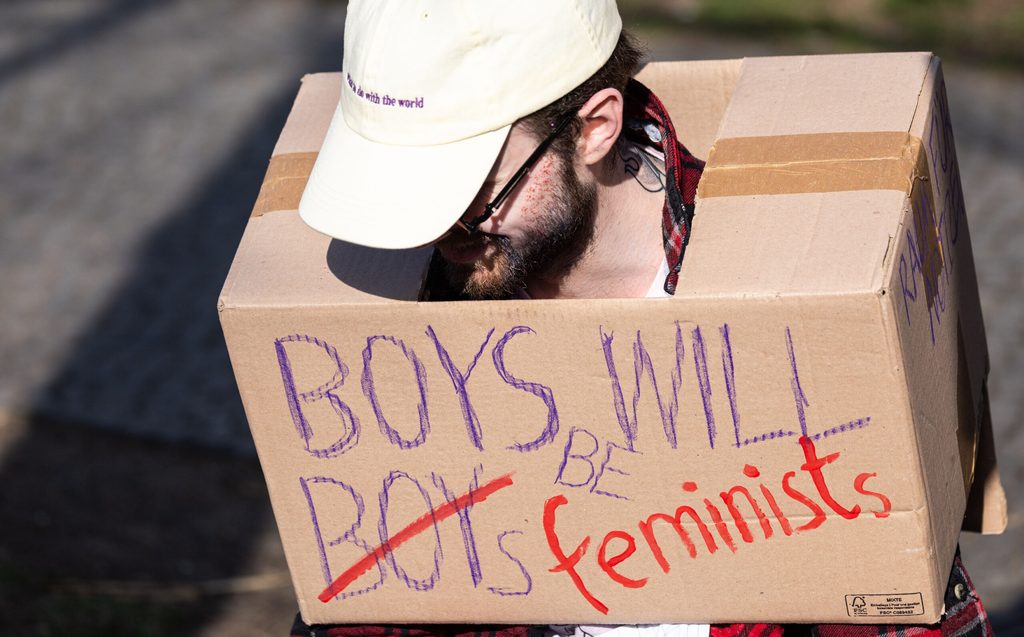 Ein Demonstrant mit einem Karton auf dem steht "Boys will be feminists“