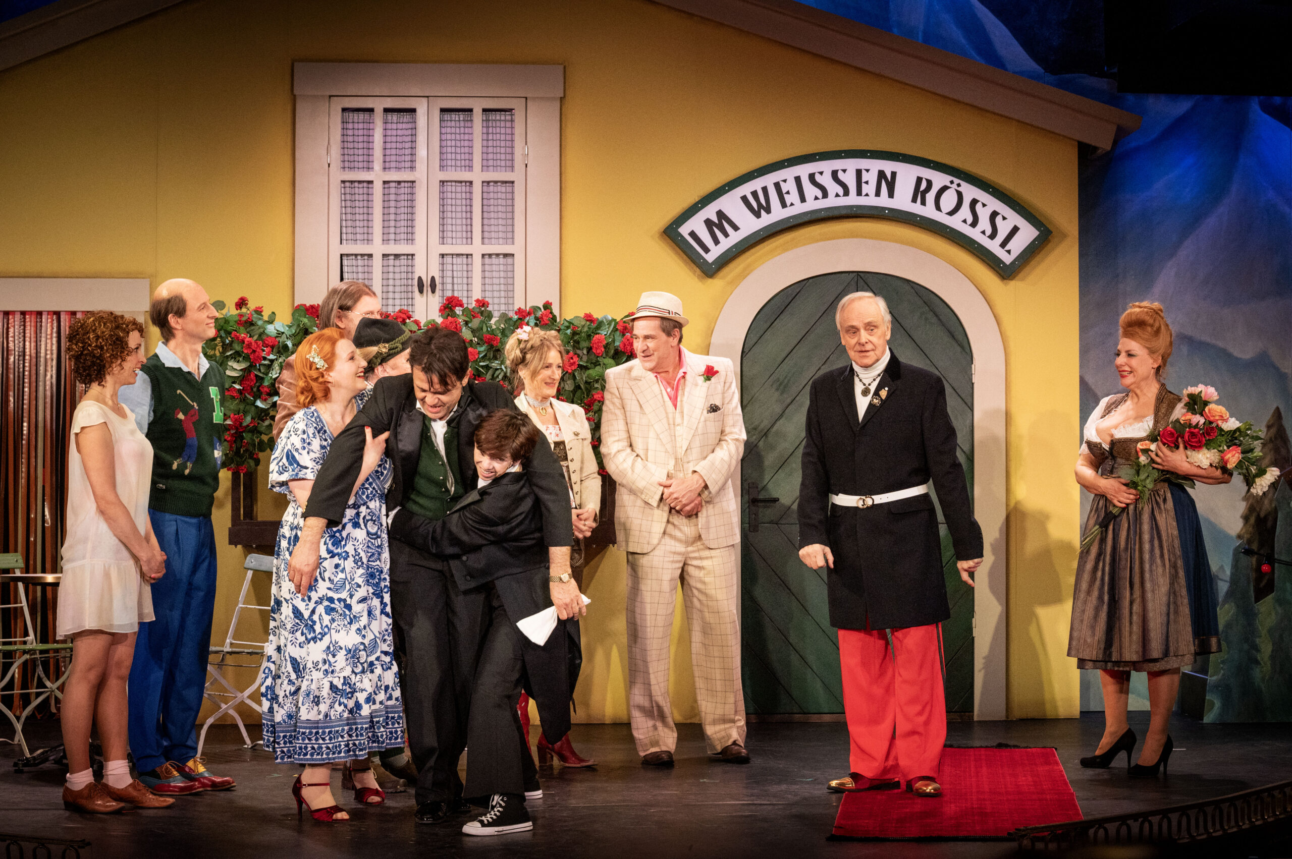 Mehrere Menschen stehen in einer Szene aus „Im weißen Rössl“ um einen Mann herum.