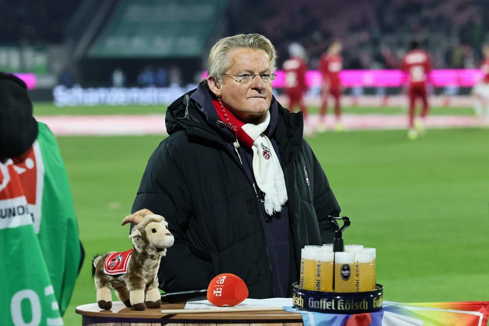 Köln-Stadionsprecher Michael Trippel steht vor einem Pult mit dem Maskottchen und ein paar Kölsch