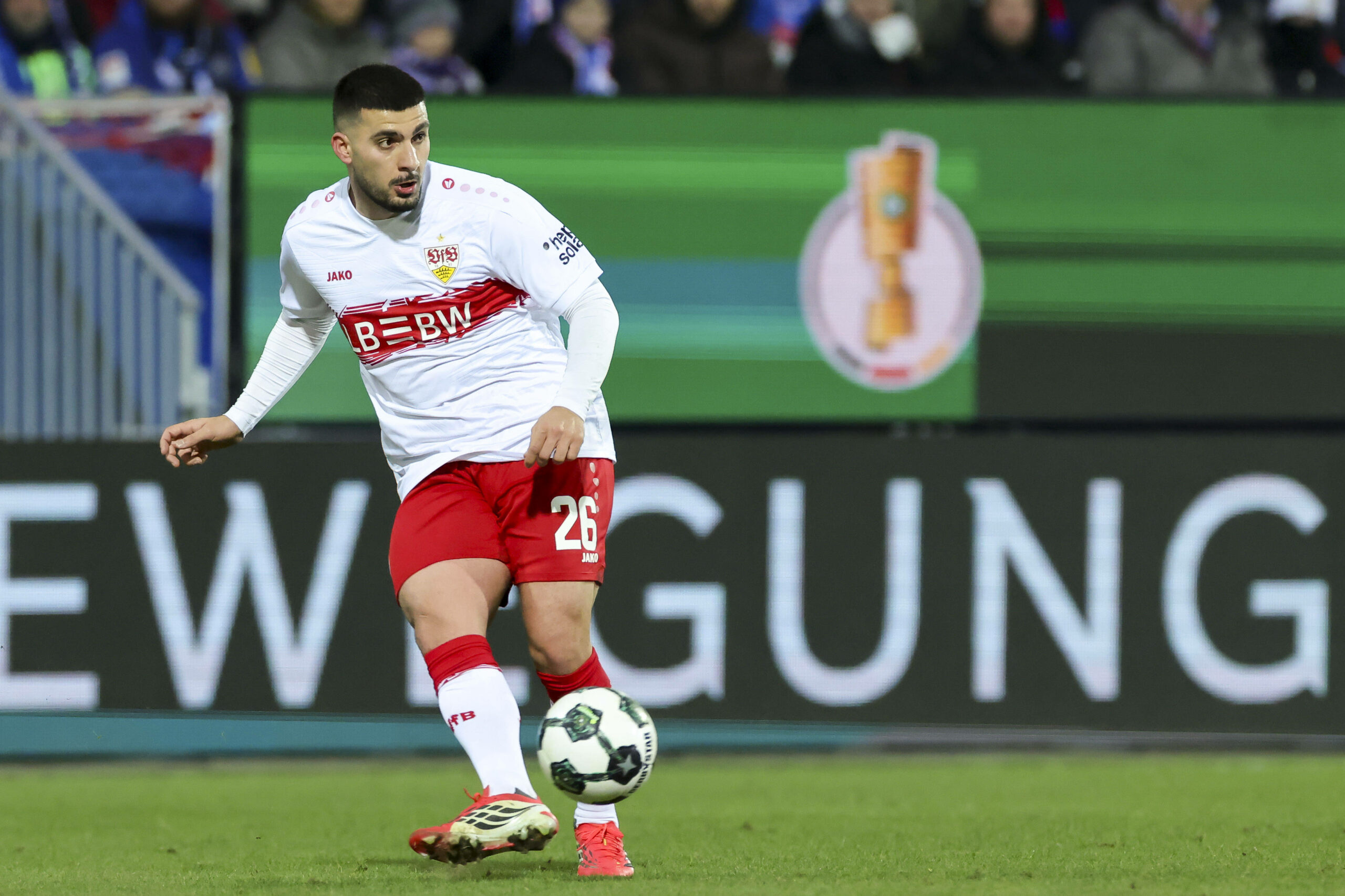 Deniz Undav spielt einen Pass, im Hintergrund ist der DFB-Pokal auf einer Bande zu sehen.