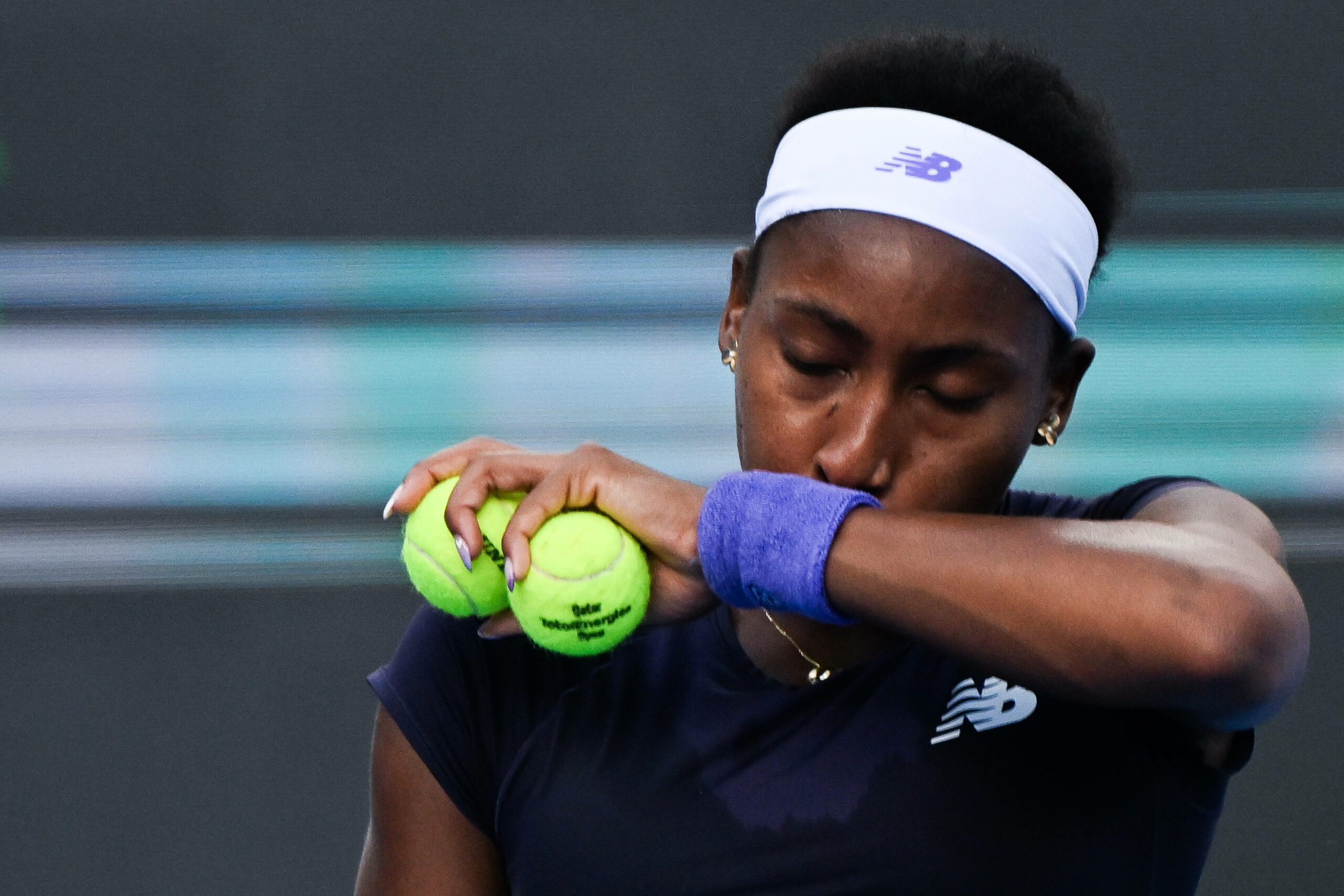 Coco Gauff wischt sich mit zwei Tennisbällen den Schweiß aus dem Gesicht und hat dabei die Augen geschlossen.