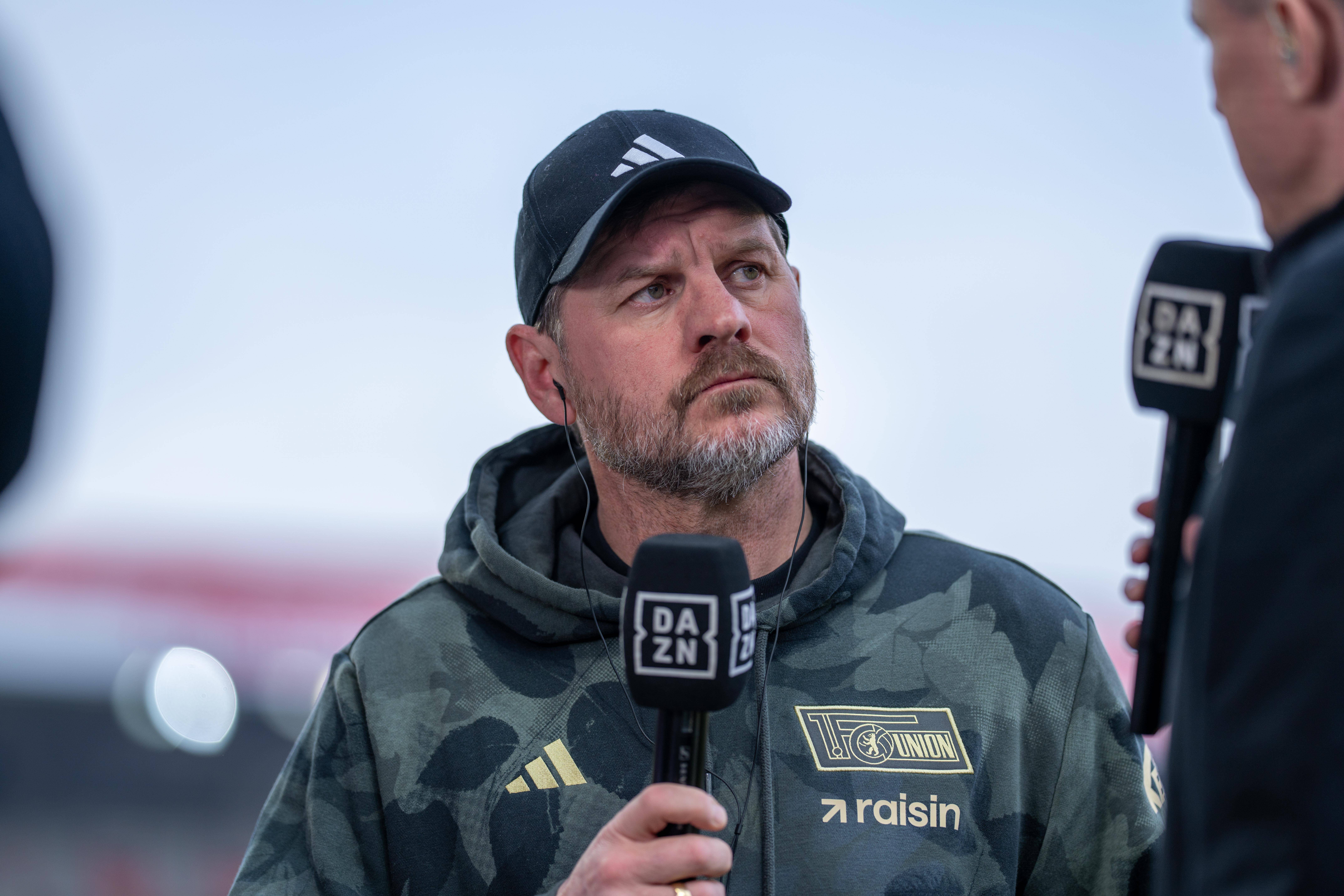Steffen Baumgart hält ein DAZN-Mikrofon in der Hand und schaut kritisch.