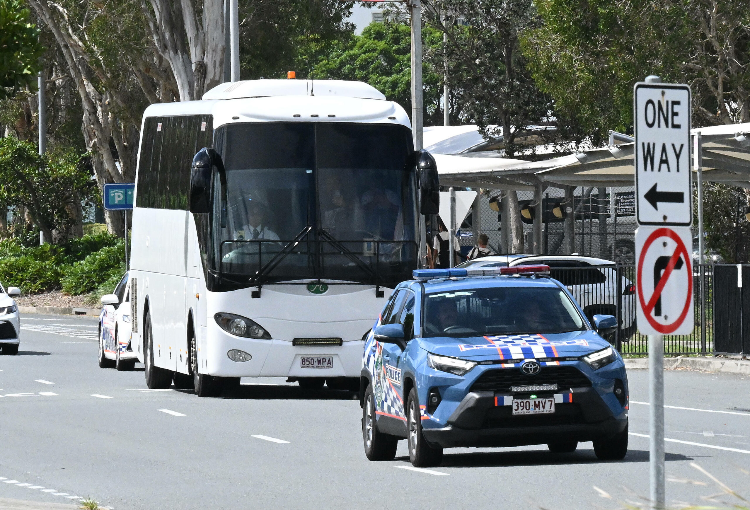 Ein weißer Reisebus wird von einem blauen australischen Polizeiauto ekortiert.