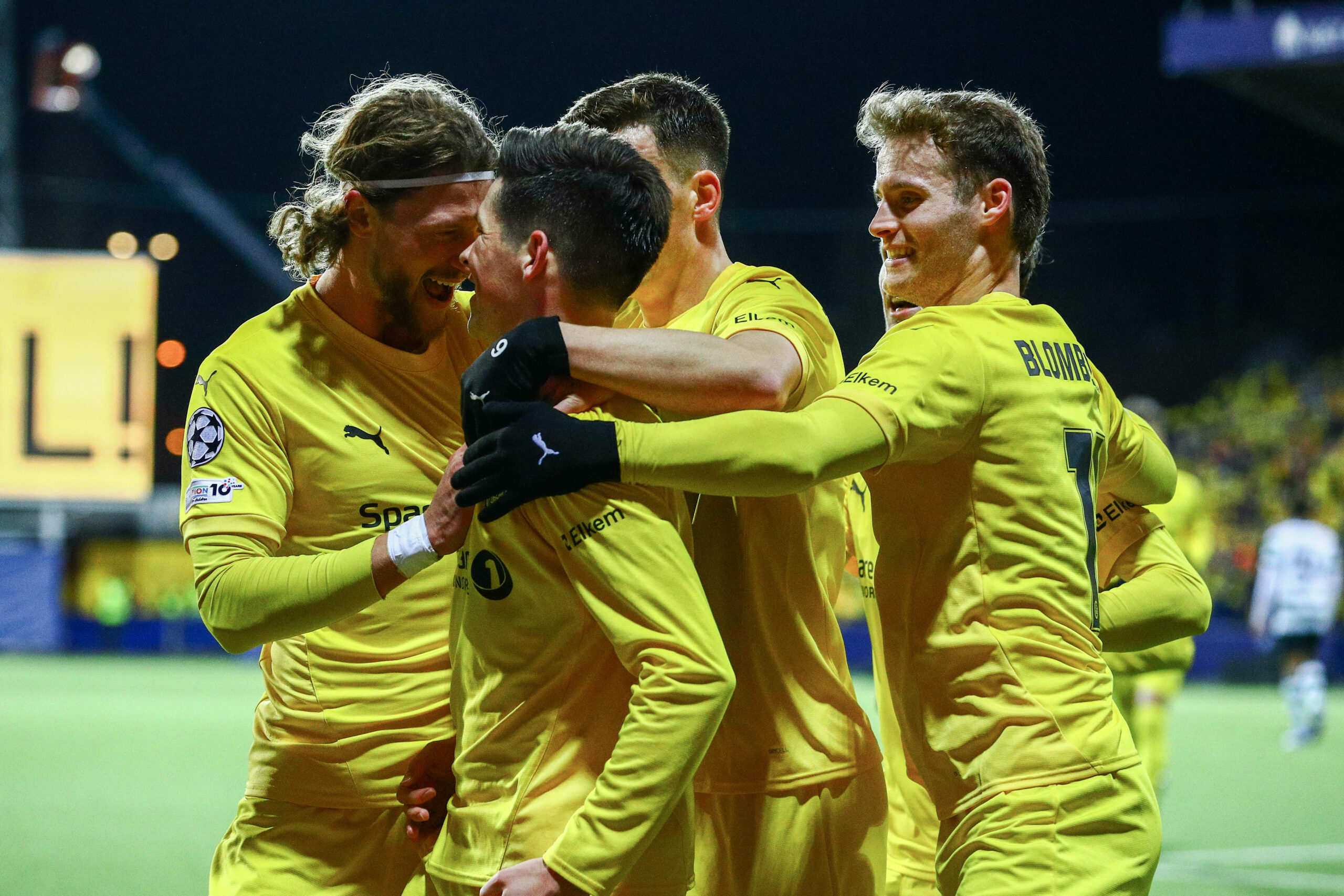 Vier Spieler jubeln in gelben Trikots in einer Traube und umarmen sich.
