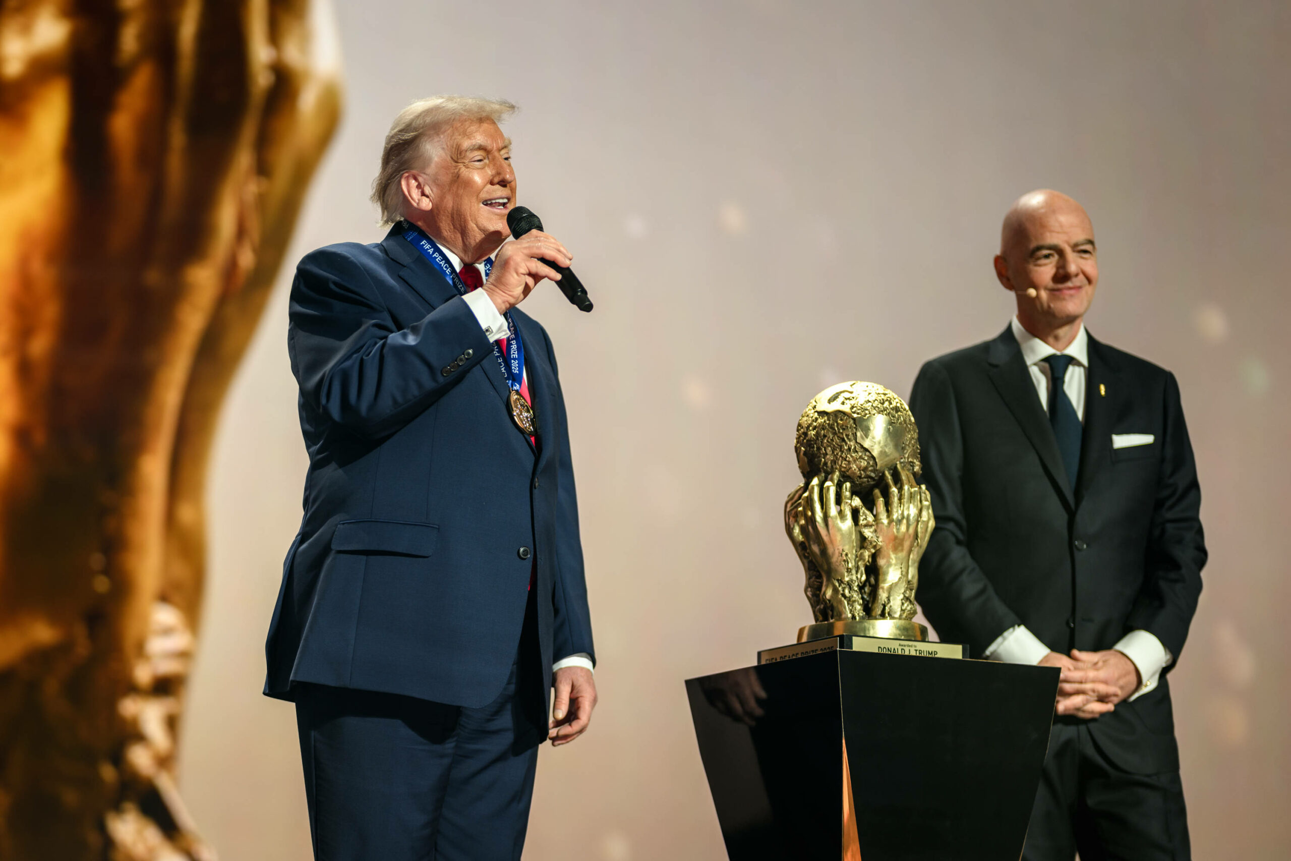 Donald Trump redet auf einer Bühne in ein Mikrofon, neben ihm Gianni Infantino.