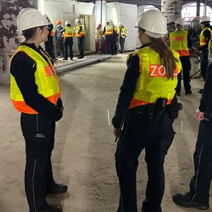 Beamte des Zolls stehen auf einer Baustelle und befragen Arbeiter.