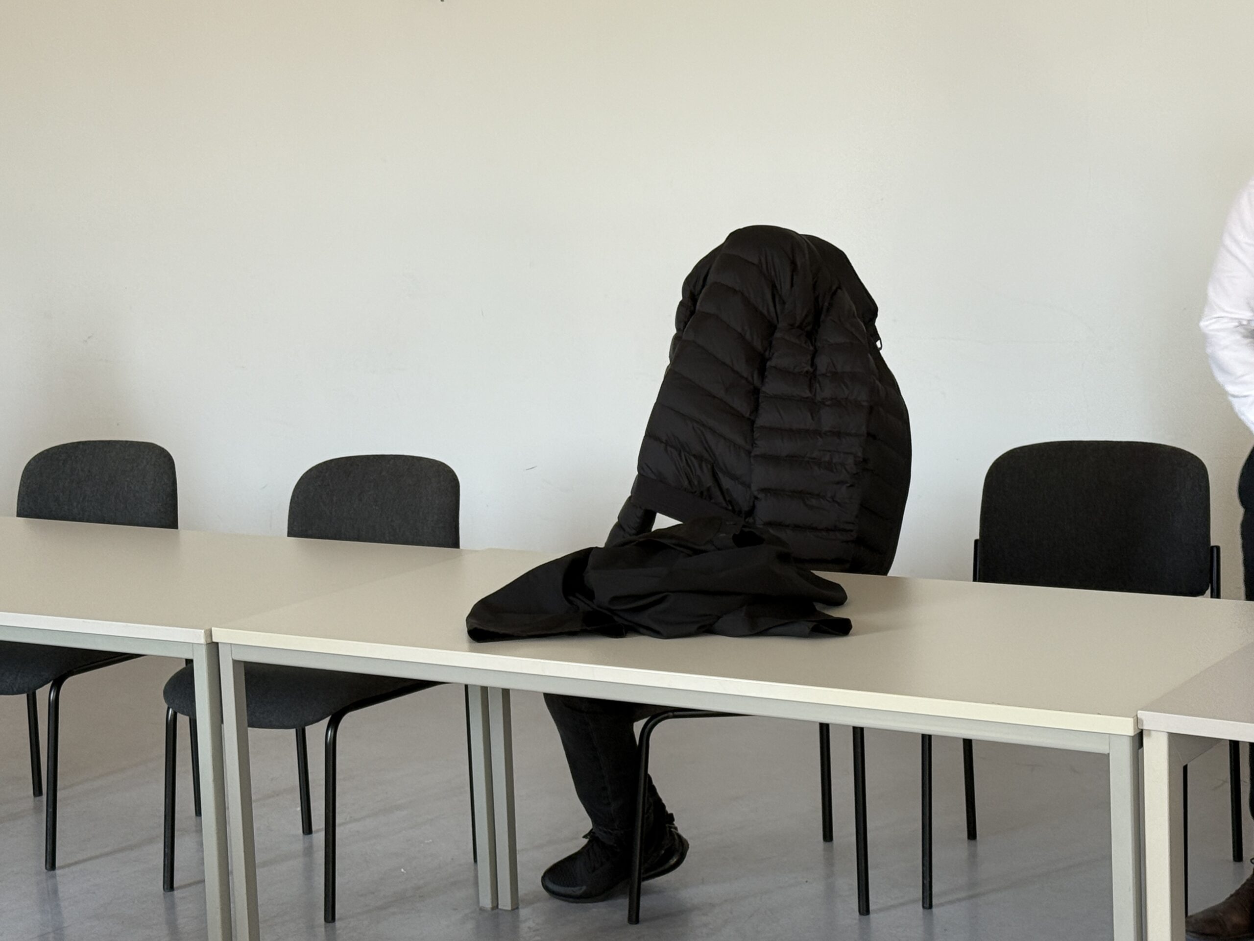 Der Angeklagte sitzt mit einer schwarzen Steppjacke über dem Kopf im Amtsgericht Altona.
