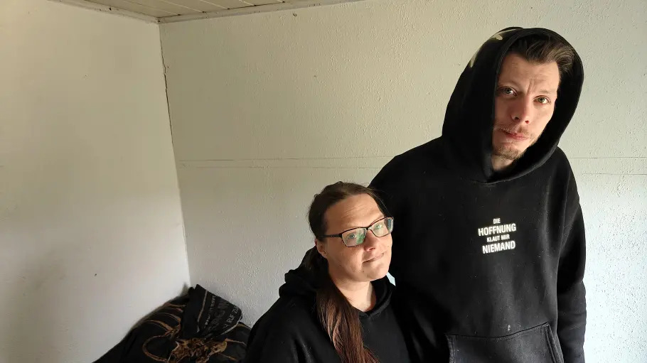 Ein Mann und eine Frau stehen vor einer weißen Wand, an der Risse zu sehen sind.