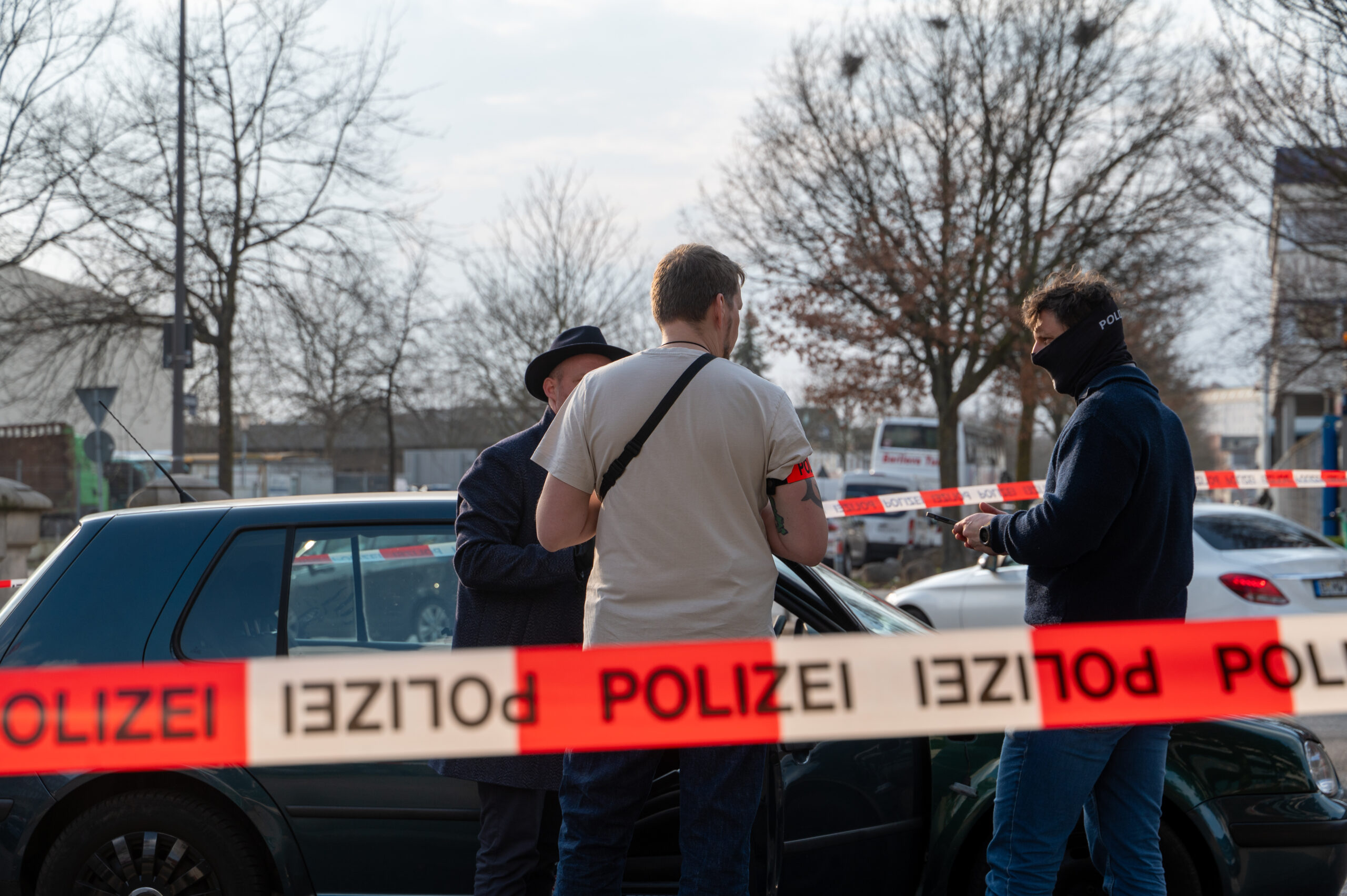 Drei Personen stehen hinter einer Absperrung auf der „Polizei“ steht.